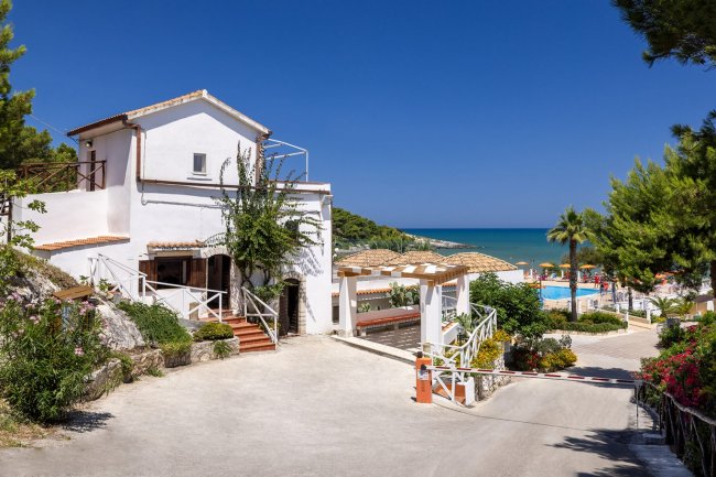 Casa bianca vicino al mare con alberi e cielo blu.