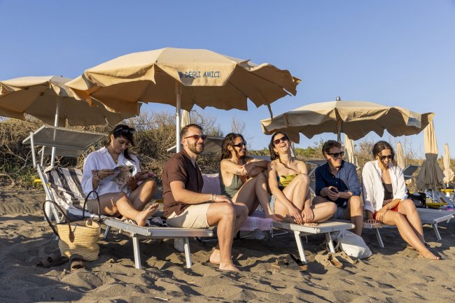 Persone sorridenti sedute sotto ombrelloni in spiaggia.