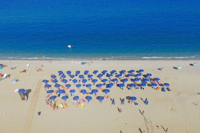 Spiaggia con ombrelloni blu vista dall'alto.