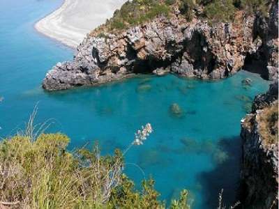Una baia con acque turchesi, rocce imponenti e un promontorio coperto di vegetazione.