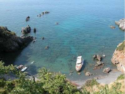 Spiaggetta con barche ormeggiate e acque limpide, circondata da rocce.