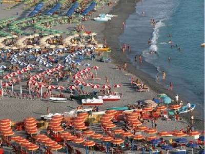 Una spiaggia affollata con file di ombrelloni colorati e persone che nuotano in mare.