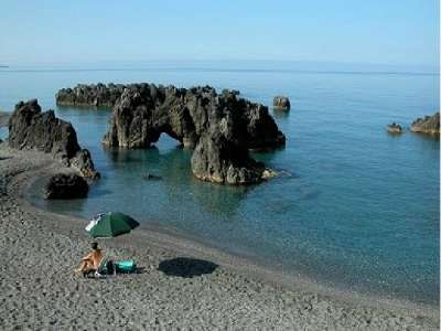 Rocce imponenti in mare con una spiaggia tranquilla, un ombrellone e una persona seduta.