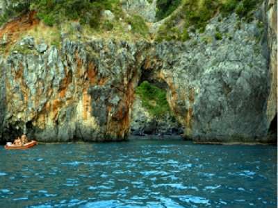 Barchetta vicino a alte scogliere con passaggio naturale.