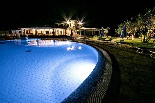 Piscina illuminata di notte con sedie a sdraio.