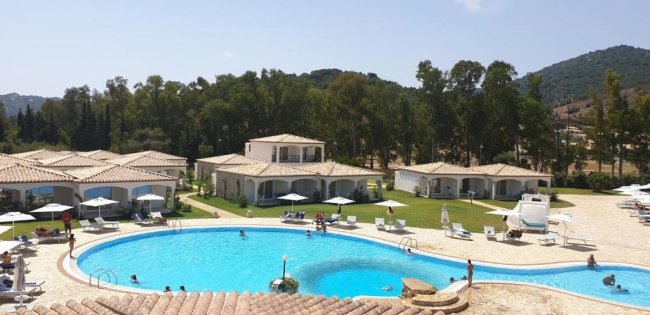 Piscina azzurra con bungalow e alberi intorno.