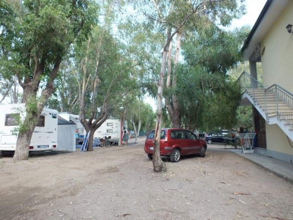 Auto e caravan vicino a un edificio, alberi sullo sfondo.