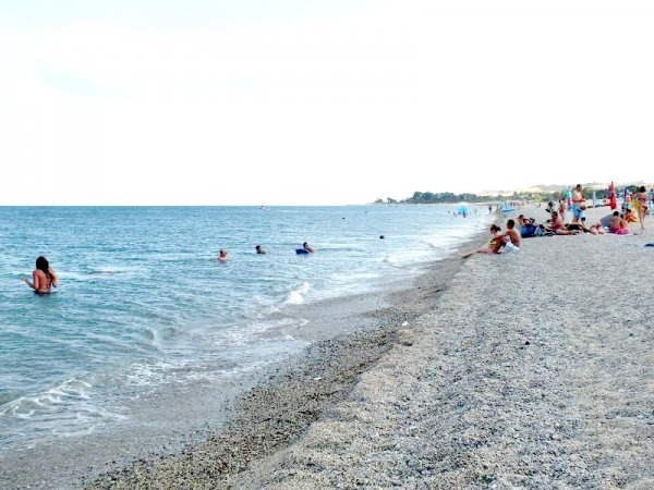 Spiaggia ghiaiosa con bagnanti e mare calmo.