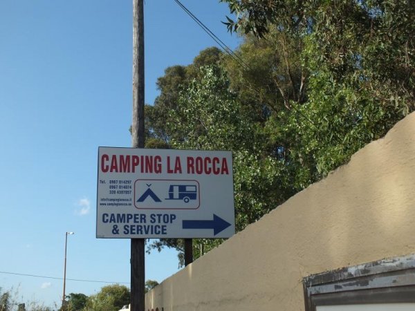 Insegna di campeggio su palo con alberi sullo sfondo.