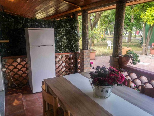 Veranda rustica con tavolo e frigorifero, vista giardino.