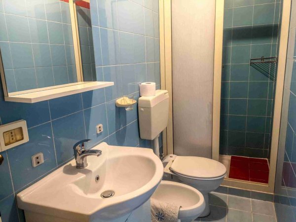 Bagno con piastrelle blu, lavandino, WC e doccia.