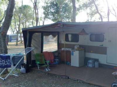Camper con veranda aperta e sedie da campeggio sotto gli alberi.