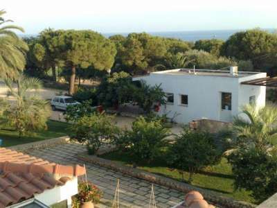 Una casa bianca circondata da alberi e vegetazione, con un'auto parcheggiata nel giardino.