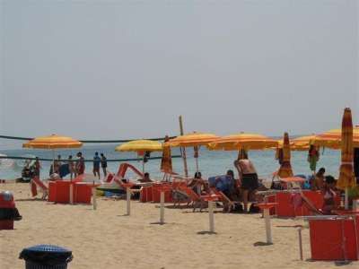 Spiaggia con ombrelloni gialli e rossi, persone rilassate e il mare sullo sfondo.