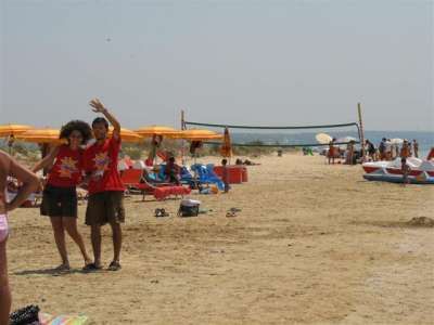 Due persone sorridenti su una spiaggia sabbiosa, ombrelloni arancioni e mare sullo sfondo.