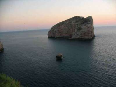 Scogliera solitaria al tramonto con mare calmo.