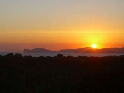 Un tramonto su un paesaggio con silhouette di colline e un cielo arancione.