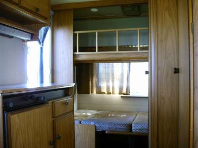 Letto a castello in una roulotte con mobile cucina a sinistra.