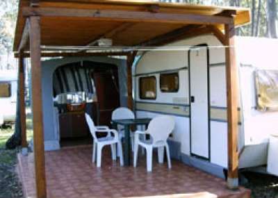 Un caravan con veranda coperta e sedie di plastica su una pavimentazione esterna.