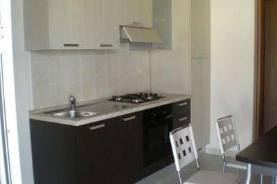 Una cucina moderna con mobili bicolore, fornelli, lavello e sedie di metallo.