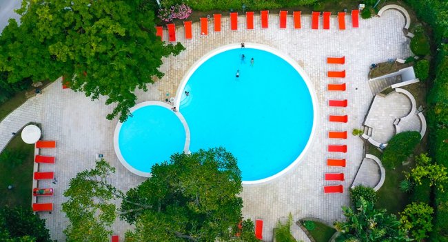 Piscina dall'alto con lettini rossi intorno.