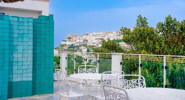 Terrazza con tavoli bianchi e vista su città collinare.