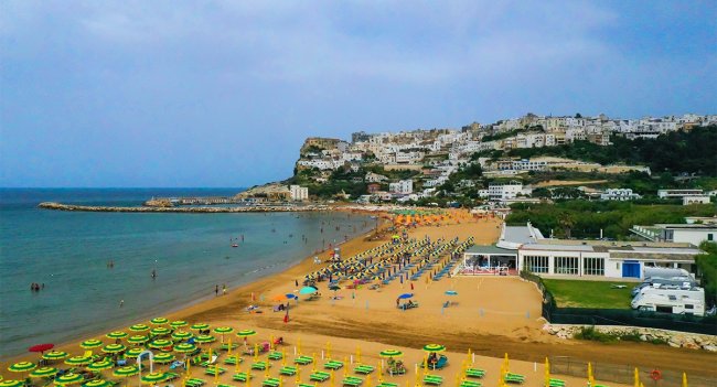 Spiaggia con ombrelloni colorati e case bianche su una collina.