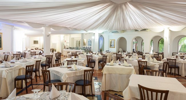 Sala con tavoli quadrati apparecchiati e soffitto drappeggiato.