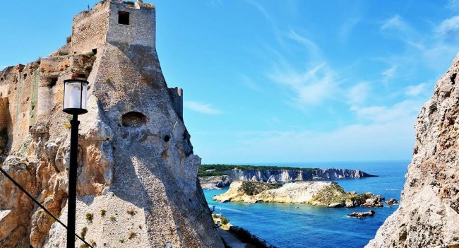 Torre di pietra su scogliera con vista sul mare blu.