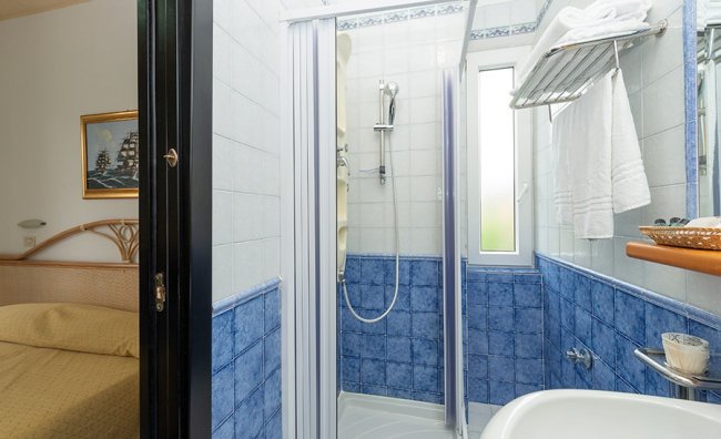 Bagno con doccia, piastrelle blu e asciugamani bianchi.
