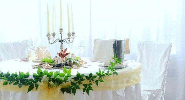 Tavolo decorato con tovaglia bianca e foglie verdi.