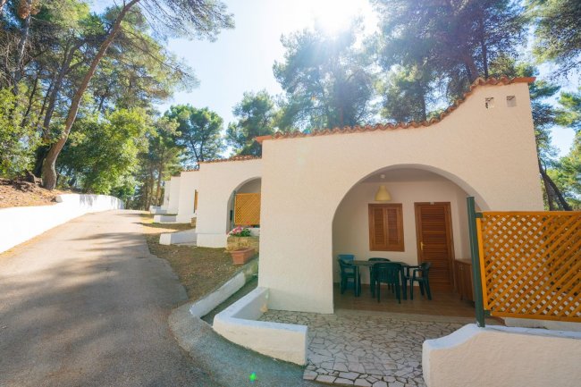 Casa bianca con veranda e sedie tra alberi.