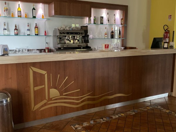 Bancone di un bar con macchina da caffè e bottiglie sugli scaffali.
