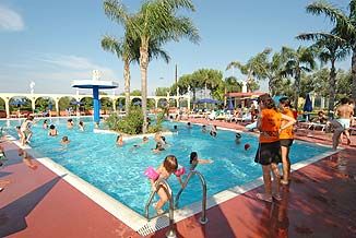 Una piscina all'aperto con persone che nuotano, circondata da palme e lettini.