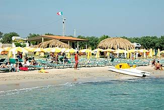Spiaggia con ombrelloni gialli, lettini, capanne di paglia e una bandiera italiana.