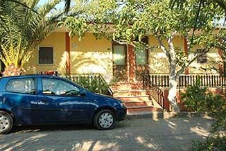 Un'auto blu parcheggiata davanti a una casa gialla con alberi attorno.
