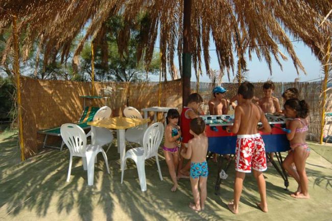 Bambini giocano a biliardino sotto una tettoia di paglia.