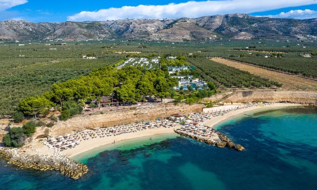 Spiaggia affollata con mare blu e colline sullo sfondo.
