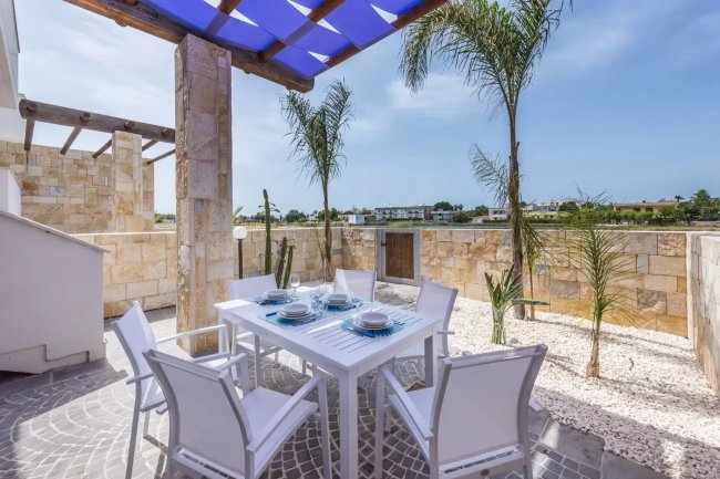 Tavolo da pranzo all'aperto sotto pergola con palme.