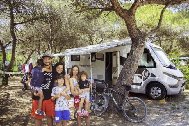 Famiglia davanti a un camper tra gli alberi.