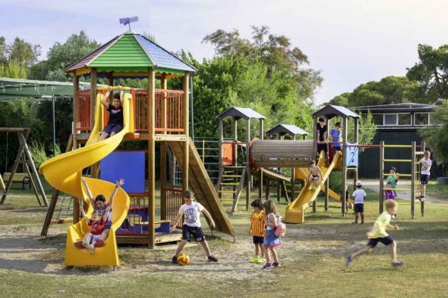 Parco giochi con bambini su scivoli e altalene.