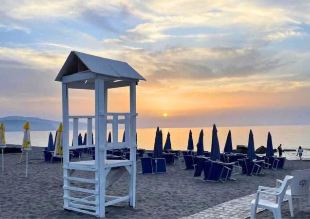 Torretta bianca sulla spiaggia al tramonto, ombrelloni blu chiusi.