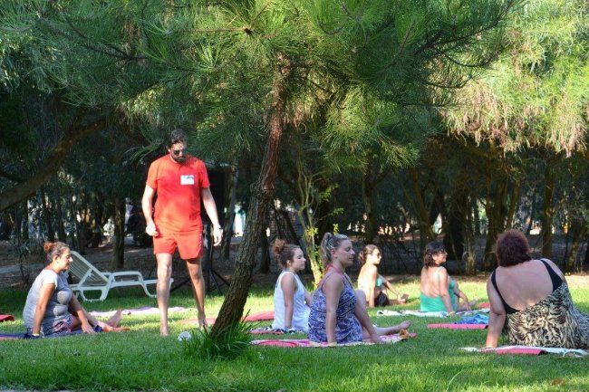 Gruppo fa yoga sul prato, istruttore in piedi, alberi sullo sfondo.