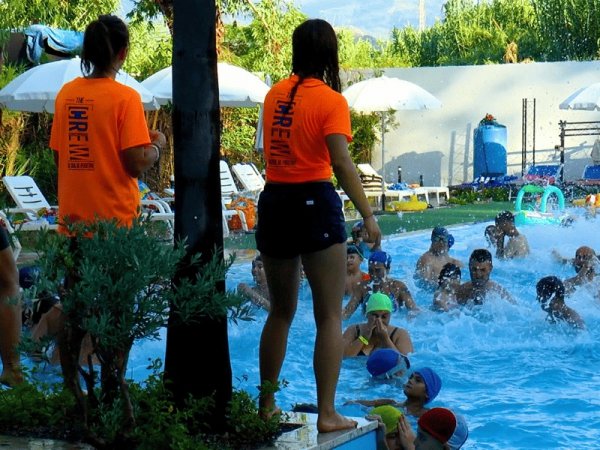 Due istruttori in magliette arancioni osservano i nuotatori in piscina.