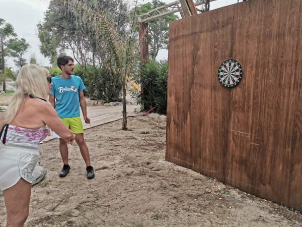 Due persone giocano a freccette all'aperto su un bersaglio di legno.
