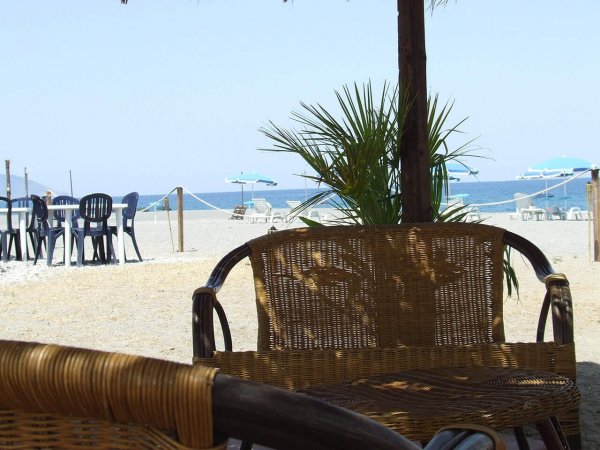 Sedie di vimini su una spiaggia con ombrelloni e vista sul mare.