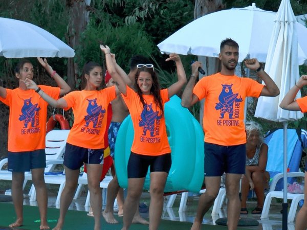 Un gruppo di persone in magliette arancioni esegue una danza all'aperto.