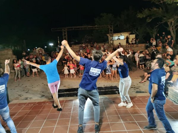 Spettacolo serale all'aperto con persone che ballano sul palco davanti a un pubblico.