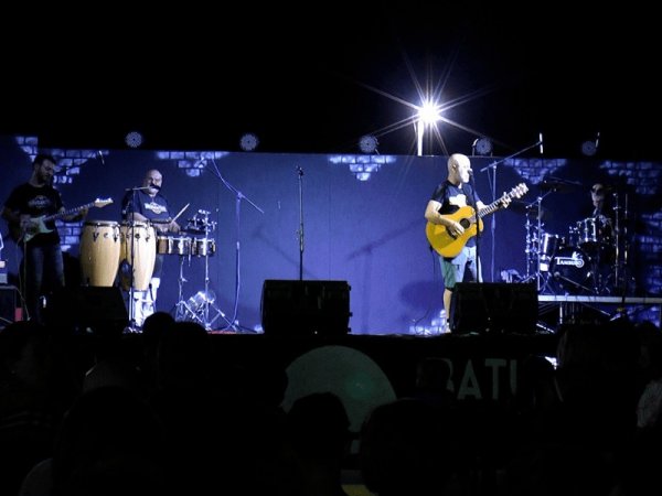 Band che si esibisce su un palco con chitarra, percussioni e batteria.