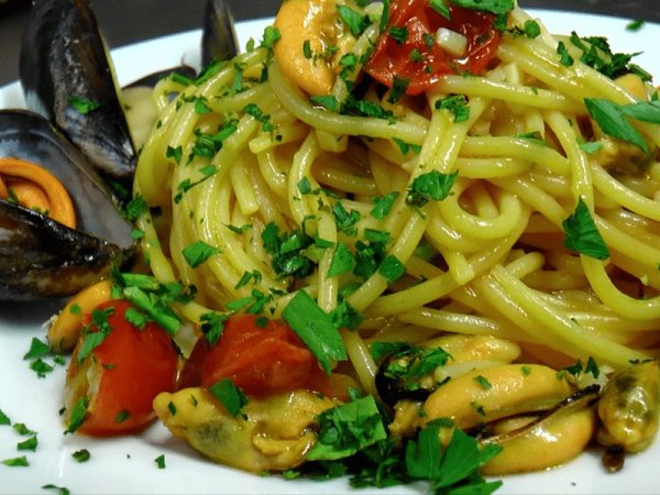 Un piatto di spaghetti con cozze, pomodorini e prezzemolo fresco.